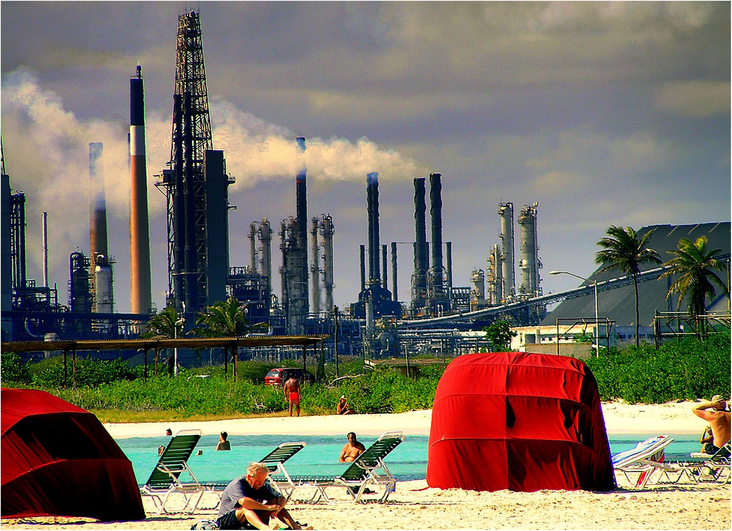 people swimming in an outdoor pool with a factory looming in the background